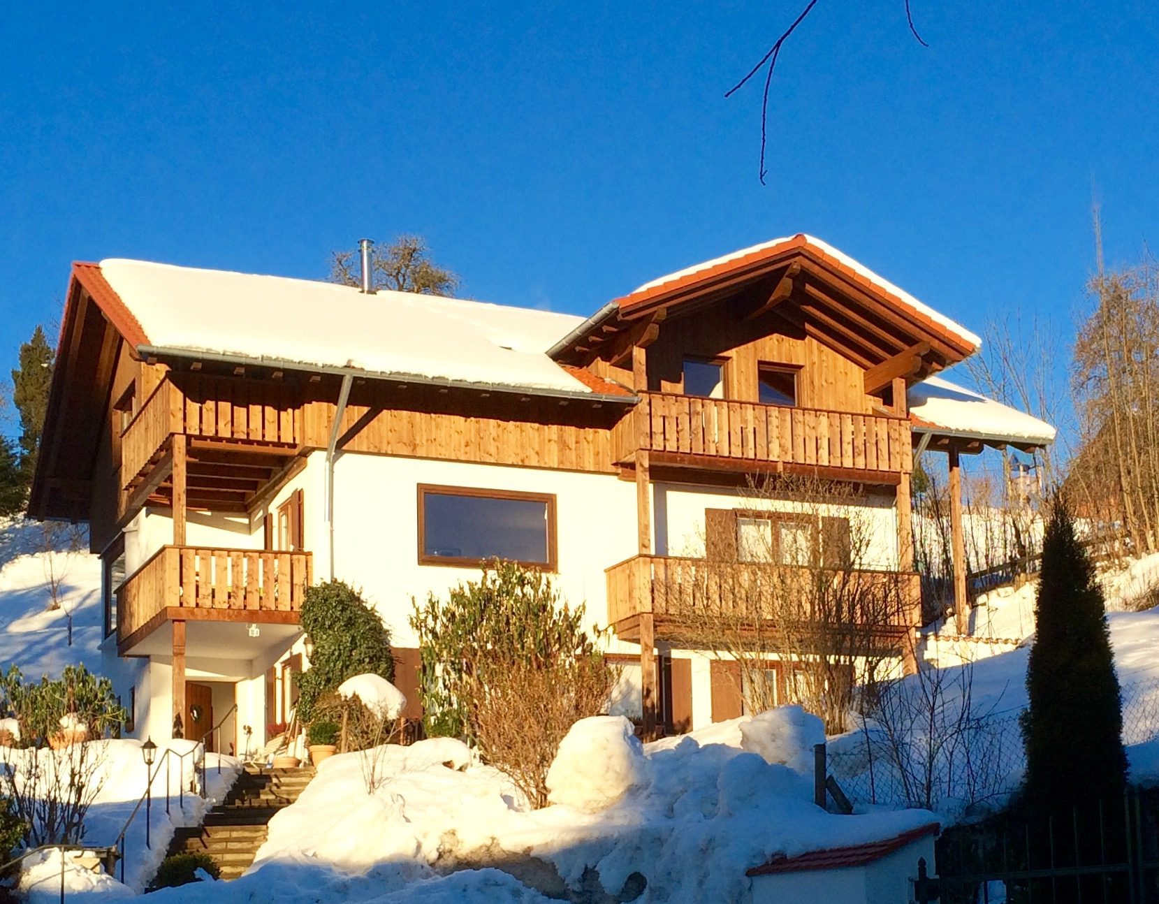 Das Haus mit Holzbalkonen im Winter, verschneiter Garten und blauer Himmel