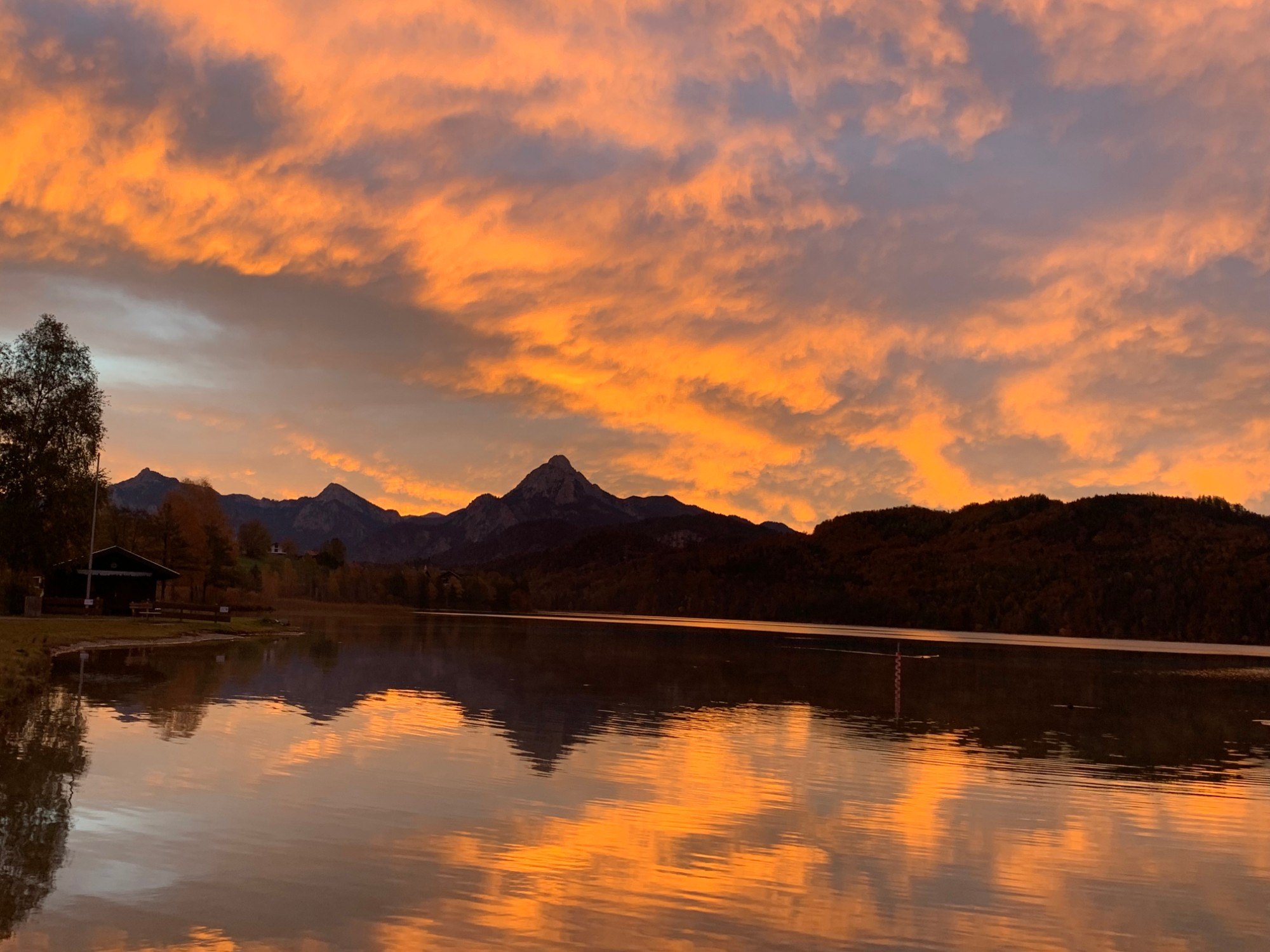 Weißensee im Abendrot, orange leuchtende Wolken spiegeln sich im See, dahinter die Berge