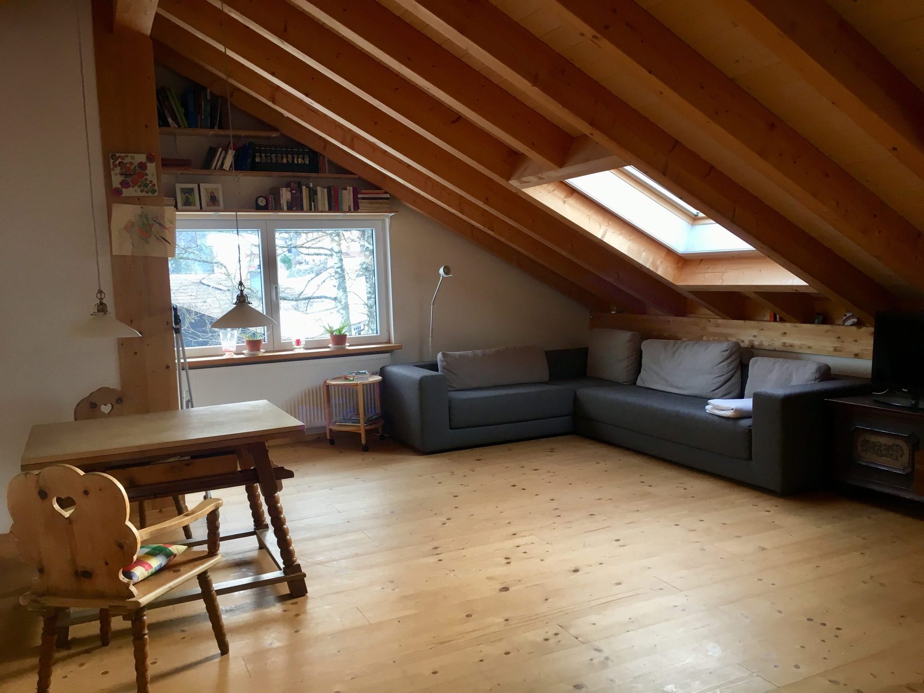 Helles Wohnzimmer unter dem Holzdach mit großem grauem Ecksofa, Esstisch und Dachfenstern